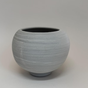 May include: A set of three ceramic mugs with a speckled, matte finish. The mugs are in shades of cream, light gray, and dark gray. Each mug has a simple, minimalist design and a rounded handle. The mugs are stacked on top of each other.