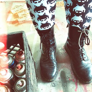May include: Black and white patterned leggings with a pixelated design. The person is wearing black leather boots with laces.