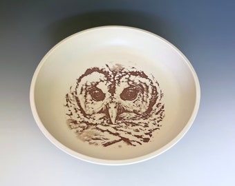 Op de afbeelding: Een witte keramische kom met een bruin uilontwerp. De ogen van de uil zijn groot en bruin, en zijn veren zijn gedetailleerd.