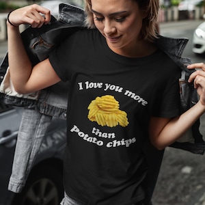 May include: A black t-shirt with the text "I love you more than potato chips" in white. A pile of potato chips is pictured above the text.