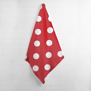 May include: A red fabric with large white polka dots hangs against a white brick wall. The fabric is folded in a triangular shape, showcasing the pattern of evenly spaced white circles on a red background. The fabric is likely a decorative item.
