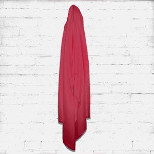 May include: A draped, solid-colored scarf in a vibrant shade of red. The fabric hangs vertically against a white brick wall, showcasing its texture and flow. The scarf's color is consistent throughout, creating a simple yet elegant aesthetic.