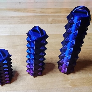 May include: Three blue and purple gradient decorative objects with a spiky, geometric design. The objects are arranged in a row, varying in size, and are set against a light brown wooden surface.