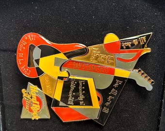 May include: A Hard Rock Cafe San Francisco guitar-shaped pin with red, yellow, black, and gold accents. The pin features the phrases "Take time to be kind," "Love all, serve all," and "Humanity is interconnected." A smaller Hard Rock Cafe pin is also included.