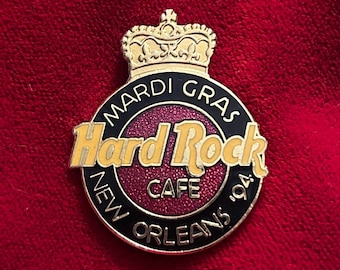 May include: A Hard Rock Cafe pin from New Orleans, '94, featuring a gold crown, the Hard Rock Cafe logo in yellow, and the words "Mardi Gras" and "New Orleans" in black. The pin has a red and black color scheme.