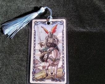 May include: A bookmark featuring a knight on horseback with wings, holding a sword. The knight is wearing armor and a helmet. The bookmark is decorated with a blue tassel.