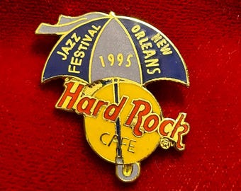 May include: A Hard Rock Cafe pin featuring a yellow and red logo with the words "Hard Rock Cafe" and "New Orleans" and "Jazz Festival 1995" on a blue umbrella design.