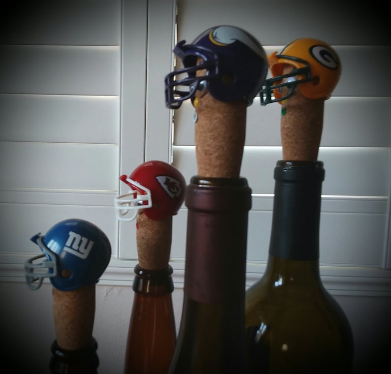 May include: Four wine bottle stoppers shaped like football helmets. The helmets are in the colors of the New York Giants, Kansas City Chiefs, Minnesota Vikings, and Philadelphia Eagles.