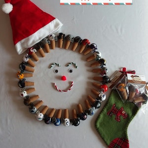 May include: A festive holiday scene with a red Santa hat, a green stocking with a red plaid cuff, and a circle of miniature football helmets on cork stoppers. The helmets are in various team colors and logos. The text "Happy Holidays!" is printed on a red and blue striped banner.