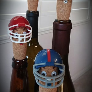 May include: Four wine bottle stoppers shaped like football helmets. The helmets are in the colors of different NFL teams: green and yellow, purple, red, and blue. The stoppers are on top of wine bottles.
