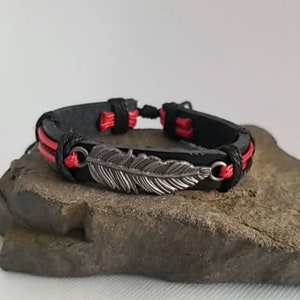 May include: A black leather bracelet with red thread accents and a silver feather charm.