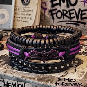 May include: A stack of black bracelets with various designs. One bracelet features a purple Batman symbol, while another has purple accents. The bracelets are stacked on a surface with the words "EMO FOREVER" visible.
