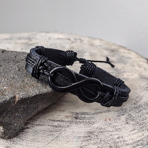 May include: Black leather bracelet with an infinity symbol charm. The bracelet is adjustable and has a braided cord detail.