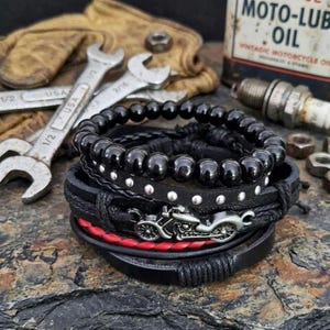 May include: A stack of black leather bracelets with silver accents and a motorcycle charm. One bracelet features red stitching. The image includes wrenches, a vintage oil can, and a spark plug.