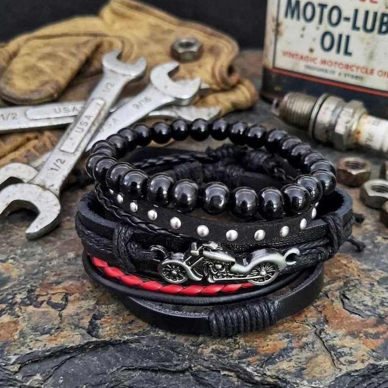 May include: A stack of black leather bracelets with silver accents and a motorcycle charm. One bracelet features red stitching. The image includes wrenches, a vintage oil can, and a spark plug.