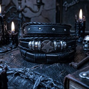 May include: A stack of black leather bracelets with silver accents. The bracelets feature braided and studded designs, with one showcasing a star-shaped embellishment. The image has a dark, gothic aesthetic, with lit candles in the background.