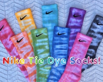 May include: Set of eight colorful tie-dye Nike socks with black Swoosh logos. The socks are arranged in a rainbow pattern, with the colors ranging from pink to blue.