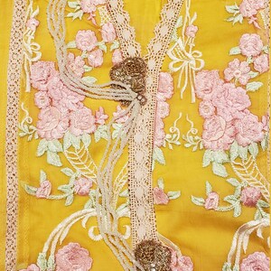 K&ouml;nnte beinhalten: Senfgelbe Tunika mit rosa Blumenstickerei und cremefarbenem Spitzenbesatz. Die Tunika hat einen V-Ausschnitt mit dekorativem Perlenbesatz. Der Markenname "AGHANOOR" steht auf dem Etikett.