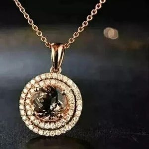 May include: A gold pendant necklace featuring a round, brown gemstone encircled by a double halo of clear, sparkling stones.