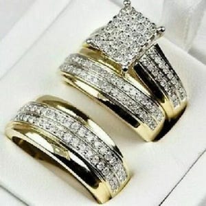 Puede incluir: Un conjunto de dos alianzas de oro con un anillo de diamantes de forma cuadrada. Las alianzas están adornadas con pequeños diamantes.