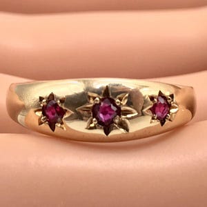May include: A gold band ring with three ruby stones set in star-shaped settings.