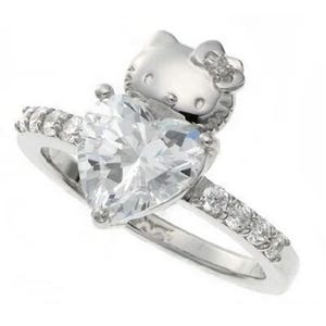 May include: A silver ring with a large heart-shaped clear crystal and a small Hello Kitty charm on top.