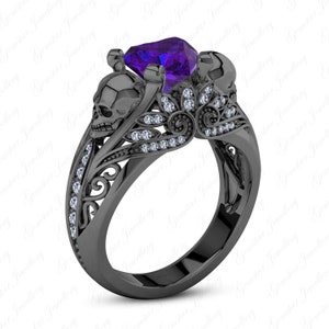 May include: Black skull ring featuring a purple gemstone and white diamonds. The ring is crafted from black metal and has an intricate design.