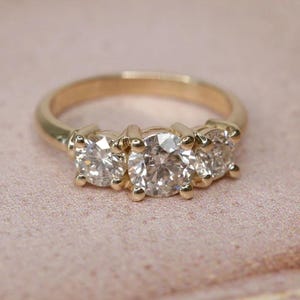 May include: A gold band ring with three round diamonds set in a prong setting.