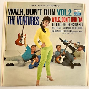 May include: Album cover for "Walk, Don't Run Vol. 2" by The Ventures. The cover features a woman in a yellow top and green pants, and several men with guitars. Text includes "Walk, Don't Run '64" and song titles.