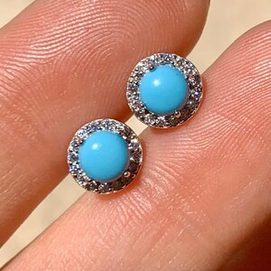 May include: A pair of silver earrings with a round blue turquoise stone set in a halo of clear cubic zirconia stones.