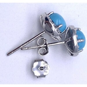 May include: A pair of silver earrings with blue turquoise stones set in a claw setting. The earrings have a post and butterfly back.