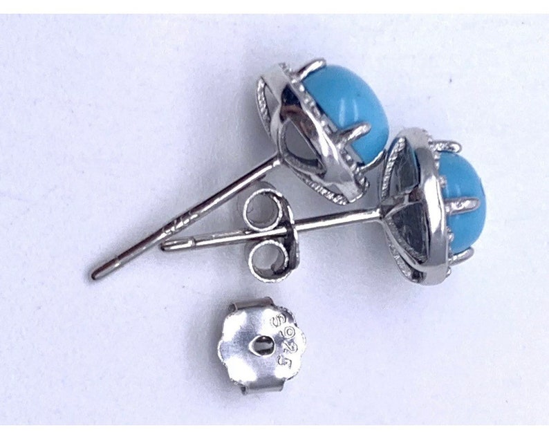 May include: A pair of silver earrings with blue turquoise stones set in a claw setting. The earrings have a post and butterfly back.