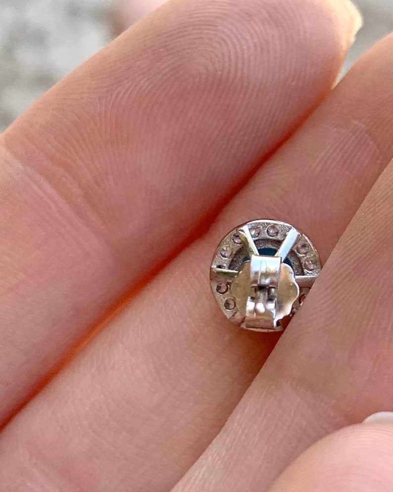 May include: Silver earring with a round, clear stone surrounded by smaller clear stones. The earring has a post back.