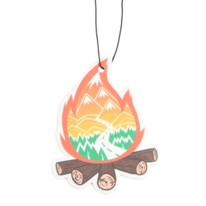 May include: A campfire-shaped air freshener with a mountain and road design. The flames are orange and red, with a white border. The mountains are orange and yellow, and the road is white. The logs are brown.