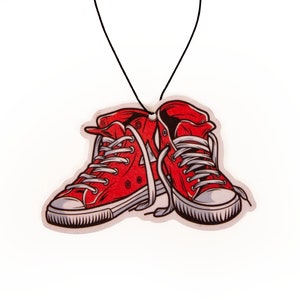 May include: Red and white cartoon sneakers hanging from a black string. The sneakers are tied together with white laces.