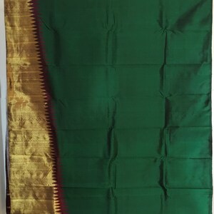 May include: A green silk saree with a gold and maroon border. The saree is folded and displayed on a white background.