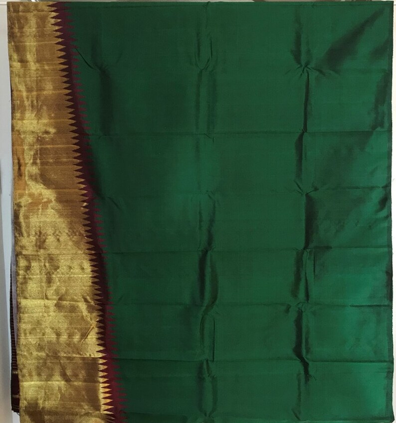 May include: A green silk saree with a gold and maroon border. The saree is folded and displayed on a white background.