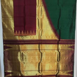 May include: A traditional Indian saree with a maroon, gold, and green color scheme. The saree features a gold border with a maroon and gold design. The pallu is maroon with a gold and orange design.