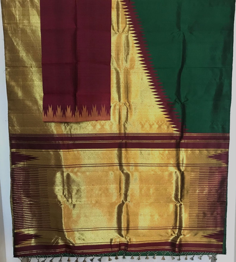 May include: A traditional Indian saree with a maroon, gold, and green color scheme. The saree features a gold border with a maroon and gold design. The pallu is maroon with a gold and orange design.