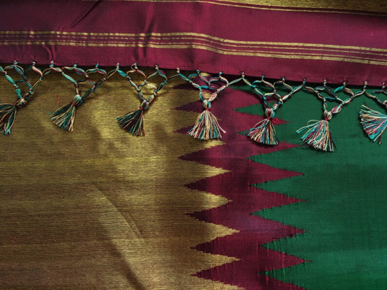 May include: A green and burgundy silk saree with gold trim and tassels. The saree has a geometric pattern and is decorated with gold thread.