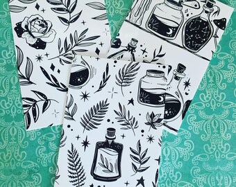 May include: Four white art prints with black illustrations. One print features a rose and leaves, another has potion bottles and candles, and the others have potion bottles, leaves, and stars. The prints are on a teal patterned background.