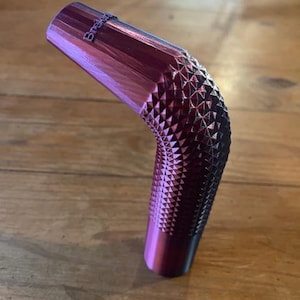 以下が含まれることがあります： ダイヤモンド模様のテクスチャードグリップが付いた、曲がったメタリックパープルのオブジェクト。「Brakes」の文字が上部に印刷されています。木製の表面に置かれたオブジェクト。