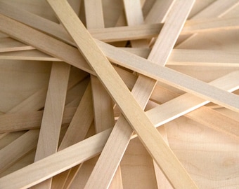 May include: A close-up view of numerous thin, light-coloured wooden strips overlapping each other. The strips are arranged in a crisscross pattern, creating a textured, layered effect. The background is a light wood surface.