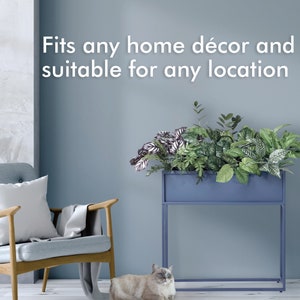 May include: A blue metal planter with various green plants, set on a matching stand. The text "Fits any home décor and suitable for any location" is displayed above the planter. A light blue chair and a cat are in the foreground.