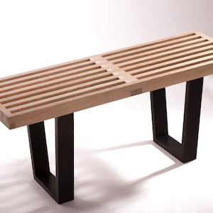 May include: A wooden bench with a slatted top and black metal legs. The bench is made of light wood and has a simple, modern design.