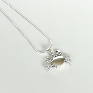 May include: A silver crab pendant necklace. The pendant features a detailed crab design with claws and legs. The necklace has a delicate silver chain. The crab pendant is approximately 1 inch wide.