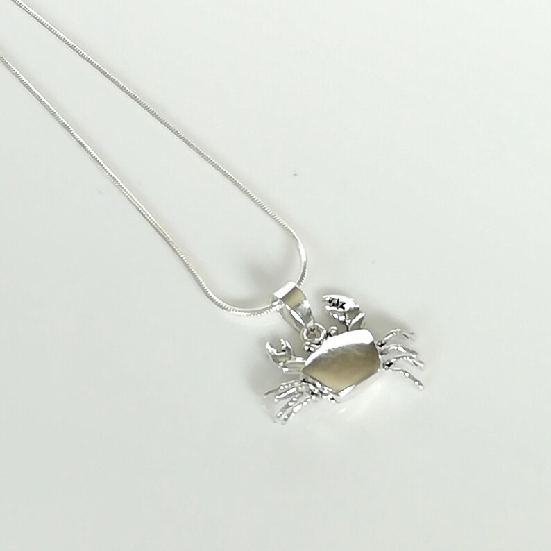 May include: A silver crab pendant necklace. The pendant features a detailed crab design with claws and legs. The necklace has a delicate silver chain. The crab pendant is approximately 1 inch wide.