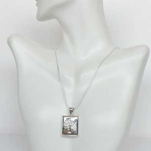 May include: A silver necklace with a square pendant featuring a detailed tree design.