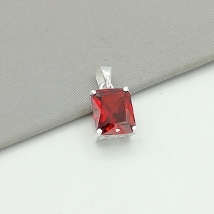 Puede incluir: Colgante rectangular de plata con una piedra preciosa roja. El colgante tiene un acabado brillante y pulido y una fianza sencilla para una cadena. La piedra preciosa es de un color rojo intenso y rico.