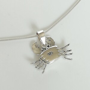 May include: A silver crab pendant necklace. The pendant is detailed with claws, legs, and a textured body. The back of the pendant is stamped with "925". The necklace chain is a thin, silver snake chain.